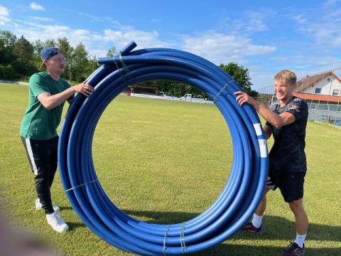 Zwei Fußballer halten ein Wasserrohr.