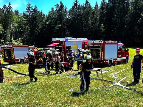 Jungfeuerwehrleute hantieren mit Schläuchen. Im Hintergrund drei Löschfahrzeuge.